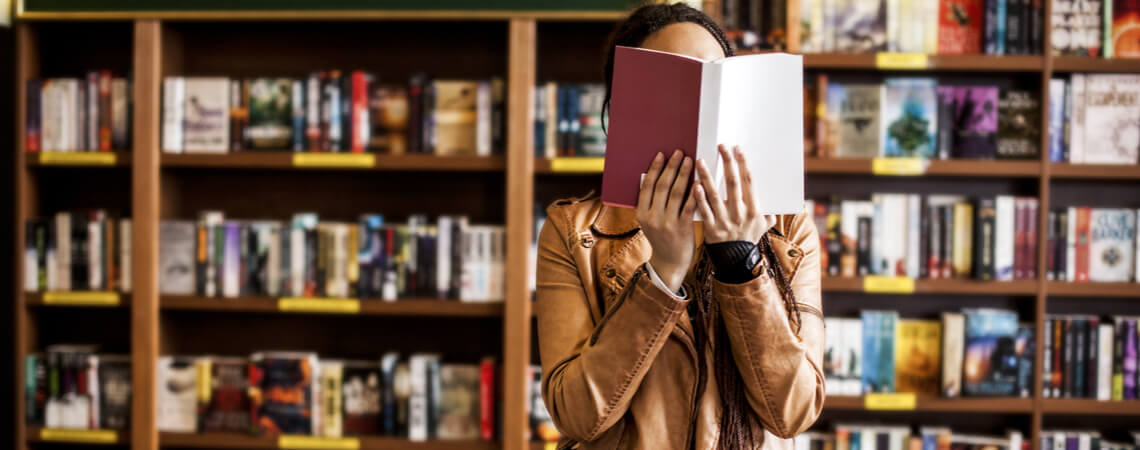 Frau in Buchladen hält sich Buch vor das Gesicht