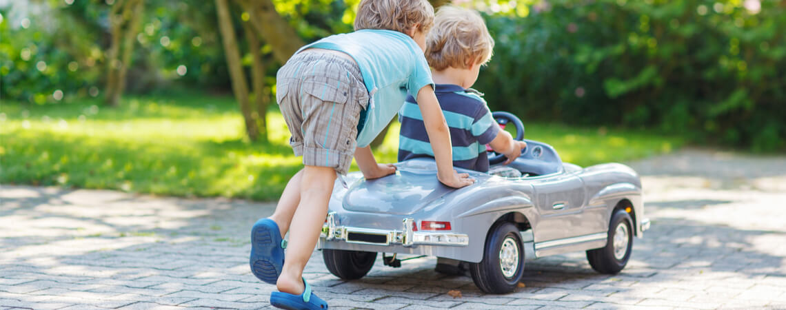 Zwei Kinder spielen draußen mit einem Elektroauto.