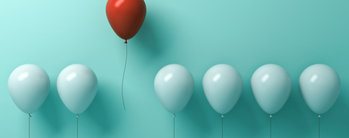 Roter Luftballon hebt sich aus eine Reihe weiser Luftballons hervor.
