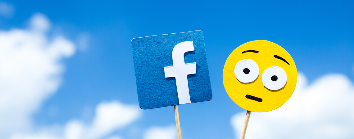 Facebook-Logo und erstaunter Smiley an Holzstab vor blauem Himmel.