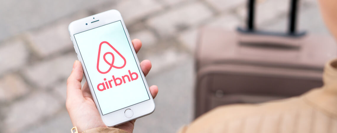 Frau hält Smartphone mit geöffneter Airbnb-App in der Hand