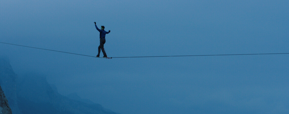 Mann balanciert auf Seil über einer Schlucht.