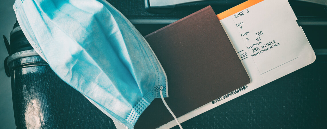 Maske und Reisepass mit Flugticket liegen auf Koffer