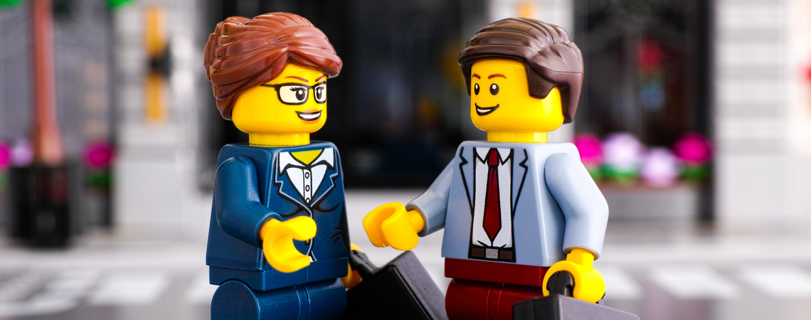 Zwei Legofiguren, die wie ein Geschäftsmann und eine Geschäftsfrau aussehen, geben sich die Hand.