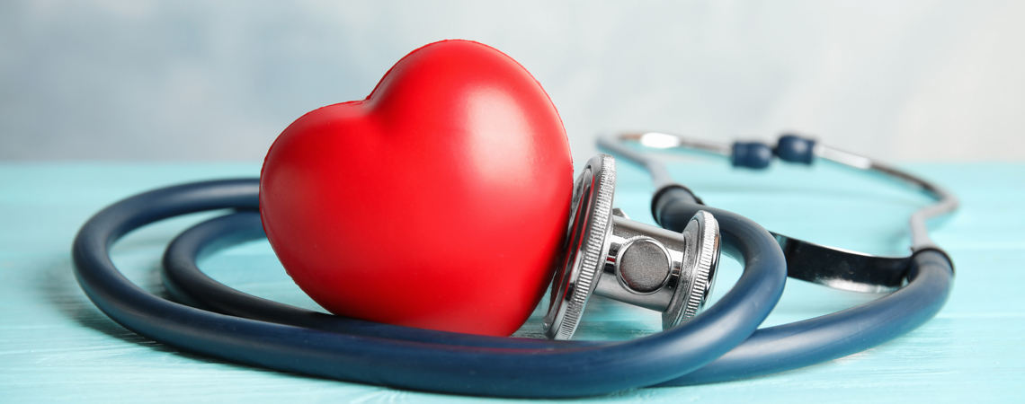Stethoskop und rotes Herz auf Holztisch