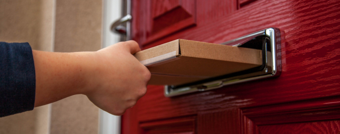 Hand schiebt Warensendung durch Briefkastenschlitz in roter Tür