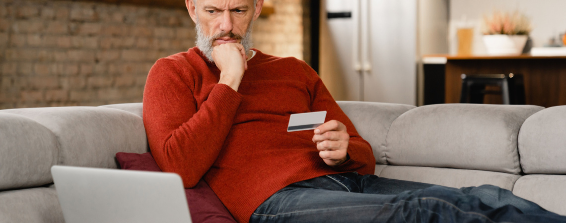 Mann sitzt rätselnd vor Laptop, mit Kreditkarte