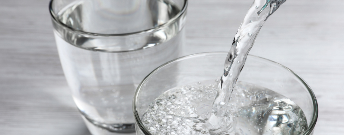 Trinkwasser aus der Flasche in Glas auf weißem Holztisch