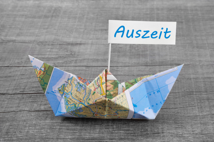 Papierschiff aus Landkarte mit einem Schild auf dem "Auszeit" steht