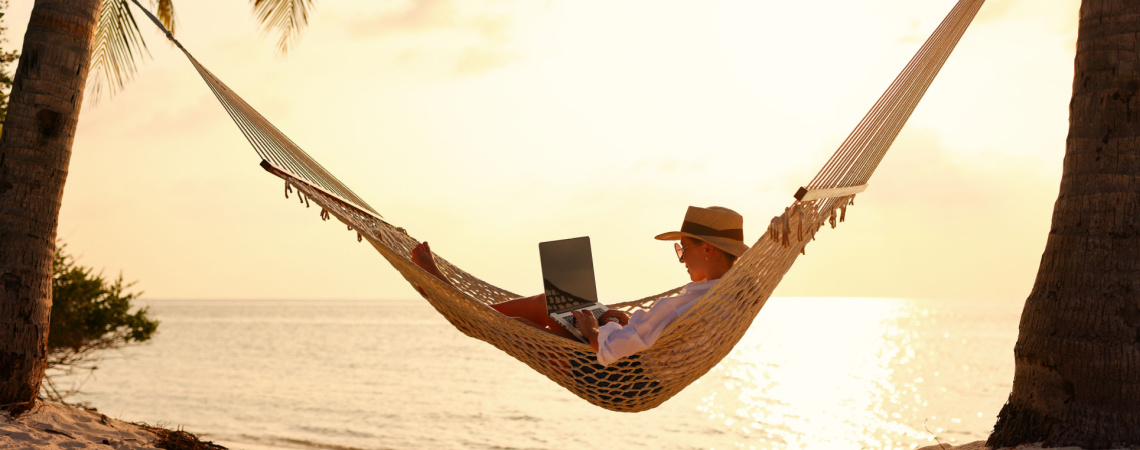 Person mit Laptop in der Hängematte am Strand
