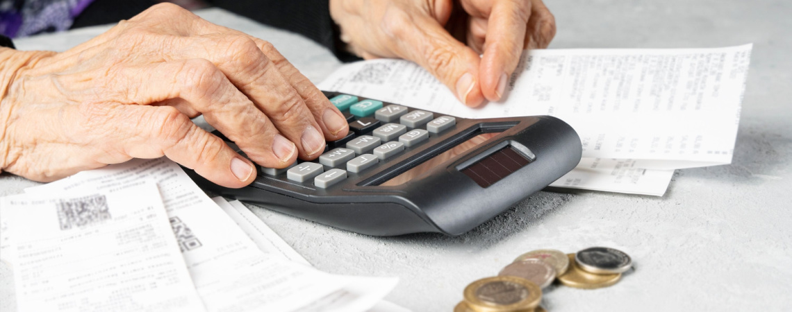 Hände eines alten Menschen rechnen Ausgaben am Taschenrechner durch
