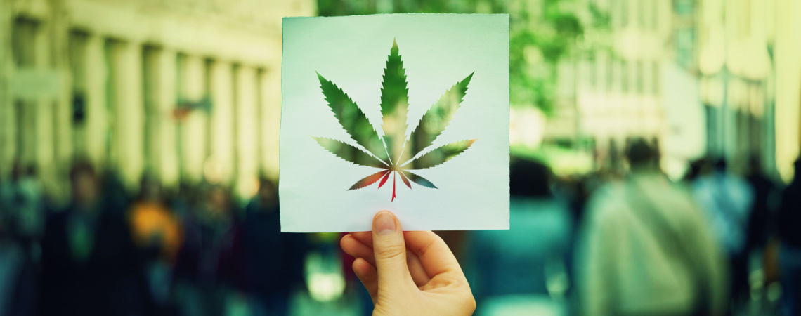 Hand hält Papierblatt mit Symbol für Marihuana-Blätter