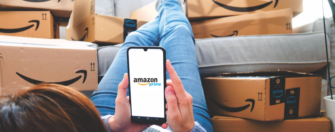 Amazon-Pakete auf Sofa und Person, die Amazon-App auf Handy öffnet