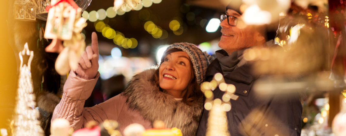 Ehepaar mittleren Alters steht vor Verkaufsstand auf dem Weihnachtsmarkt