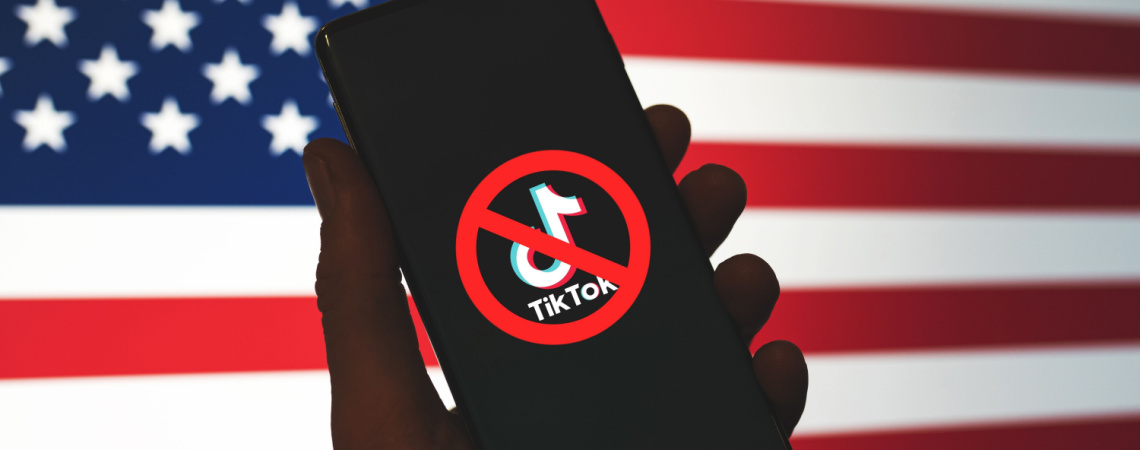 Durchgestrichenes TikTok-Logo auf Mobiltelefon vor US-Flagge