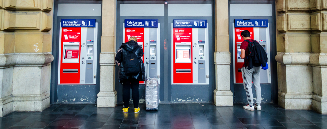 Zwei Personen stehen vor Fahrkartenautomaten im Bahnhofseingang