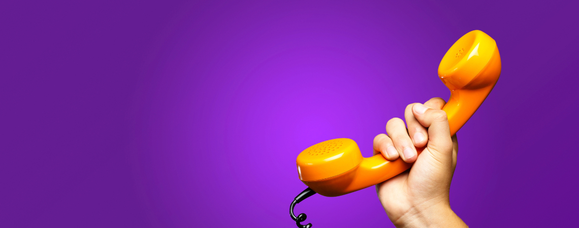 Weibliche Hand hält orangefarbenen Telefonhörer