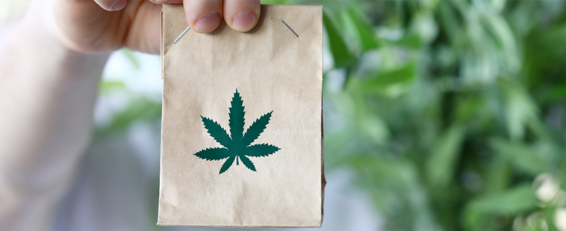 Hand hält kleine Papiertüte mit einem aufgedruckten Cannabis-Blatt