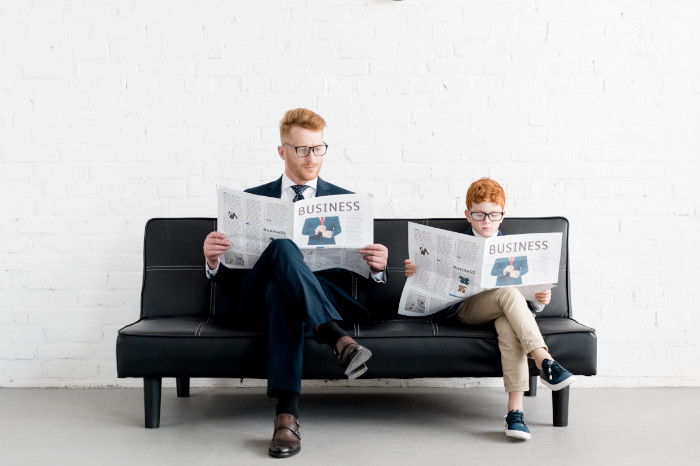 Vater und Sohn in Anzügen mit Zeitung