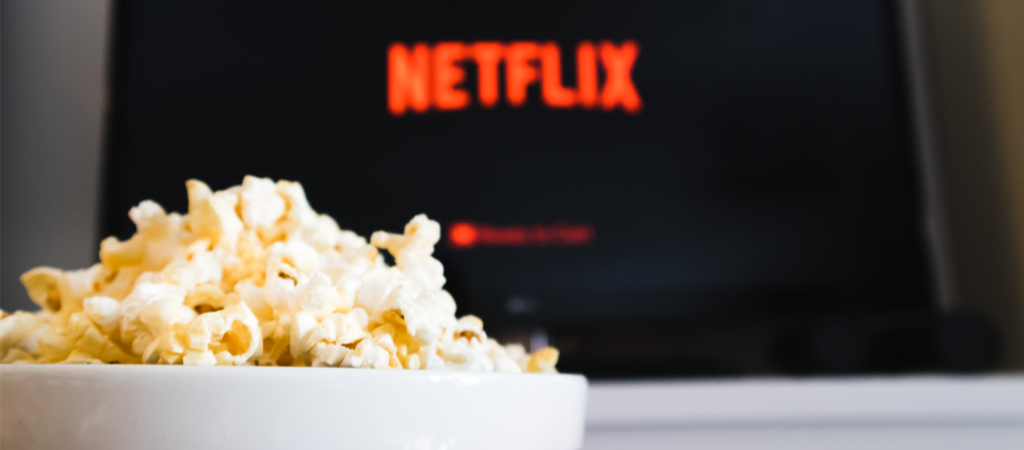 Schale Popcorn, i Hintergrund ein Bildschirm, auf dem verschwommen das Logo von Netflix zu sehen ist