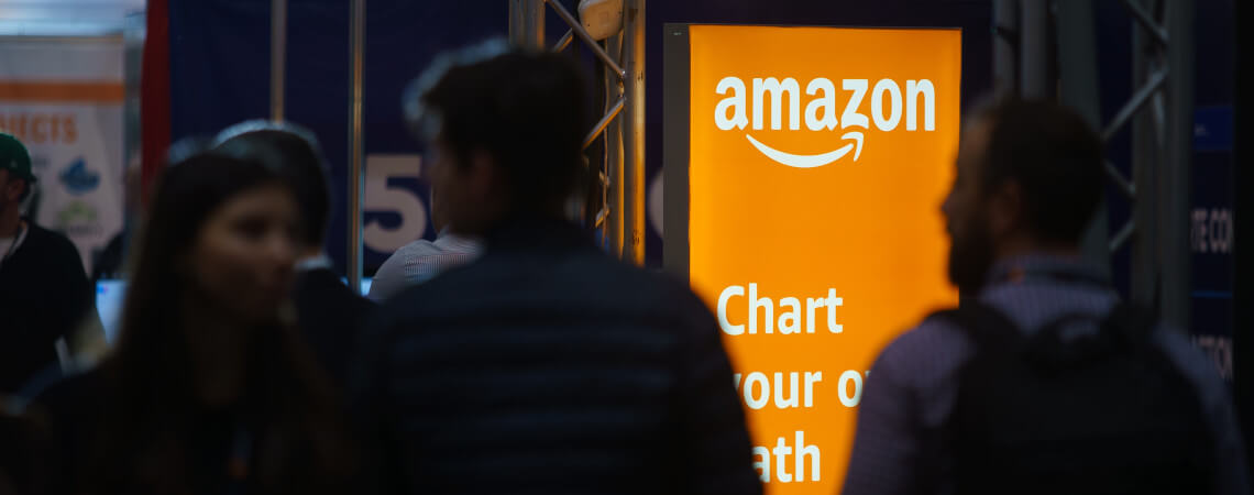 Menschen vor einem Aufsteller von Amazon: Online-Riese ändert Gehaltsstrategie 